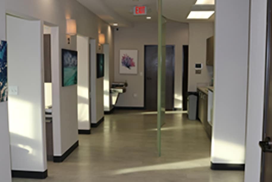 Modern dental office hallway with clean white walls, clinical lighting, and treatment rooms.