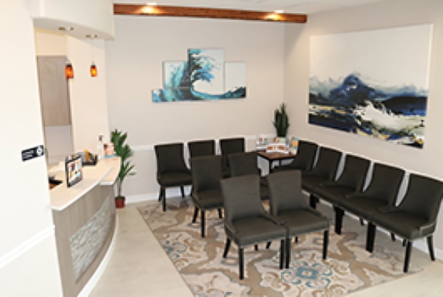 Modern dental office waiting room with black chairs, white walls, and blue landscape artwork.