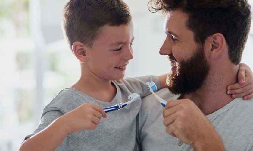Father and son brushing teeth together in bright, clean bathroom setting.
